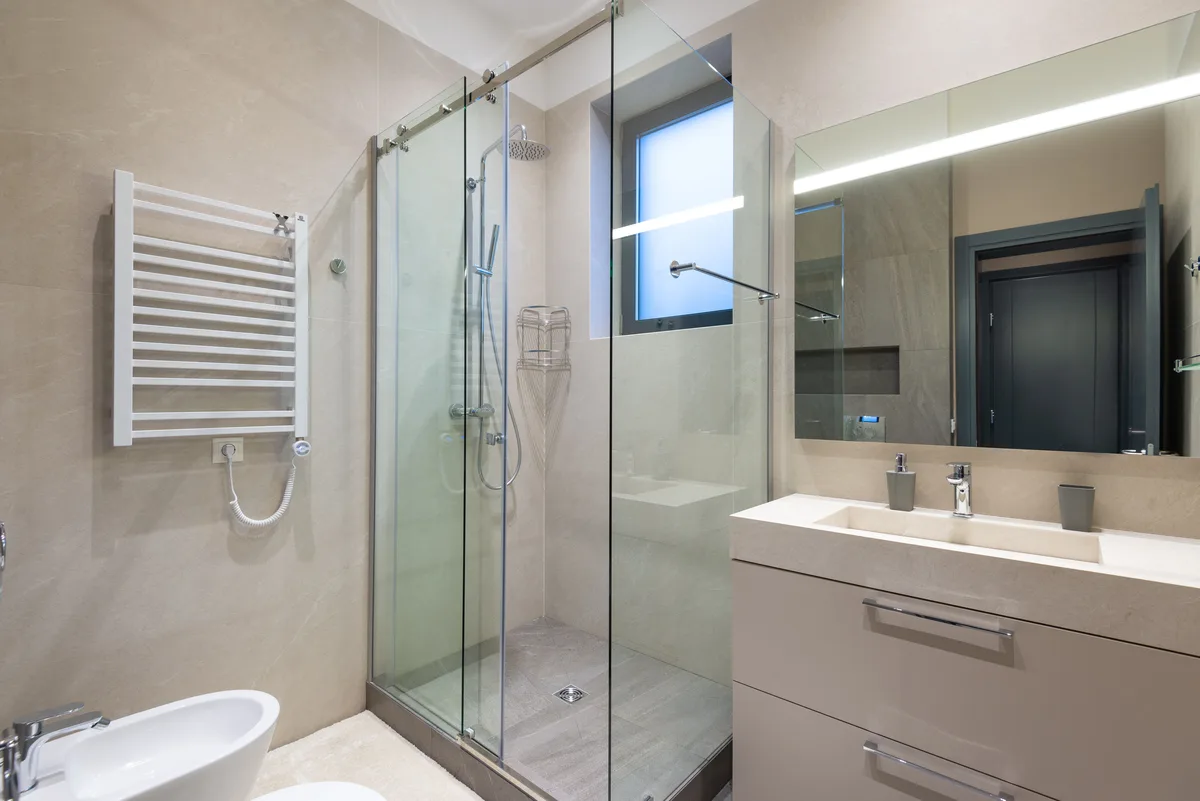 Finished bathroom with glass shower enclosure, towel radiator and vanity unit with mirror