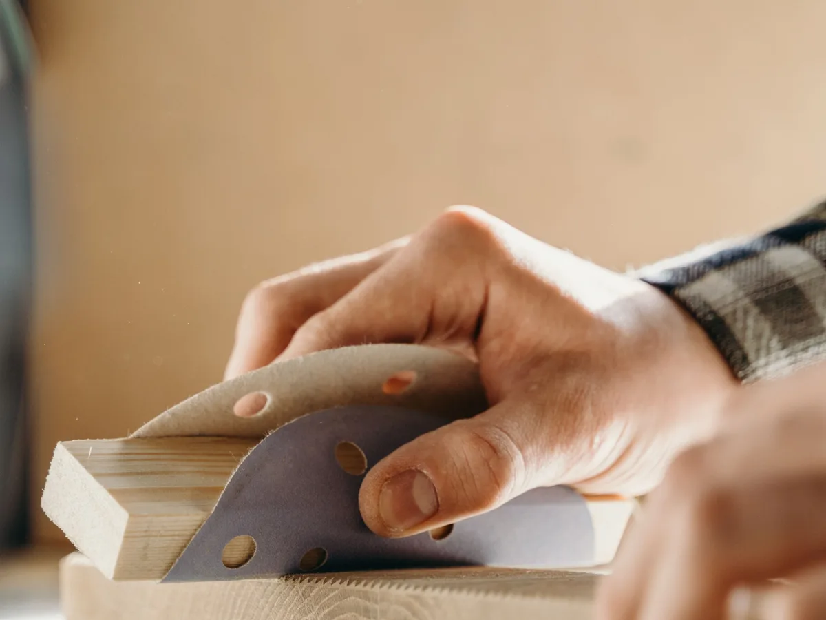 Hand sanding the edge of a wooden batten with a perforated sanding disc