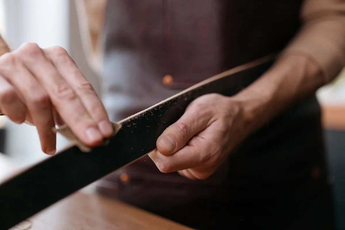 Hands sanding a dark wooden batten with a folded piece of sandpaper, with the sanding dust clearly visible