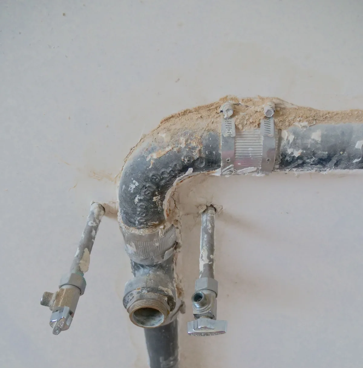 Old water pipes protruding from a wall, with two small shut-off valves and a waste elbow during a renovation