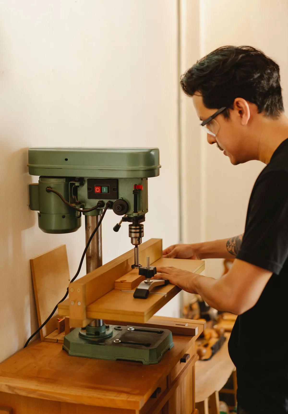 Man wearing safety glasses drilling a square hole in a workpiece with a pillar drill