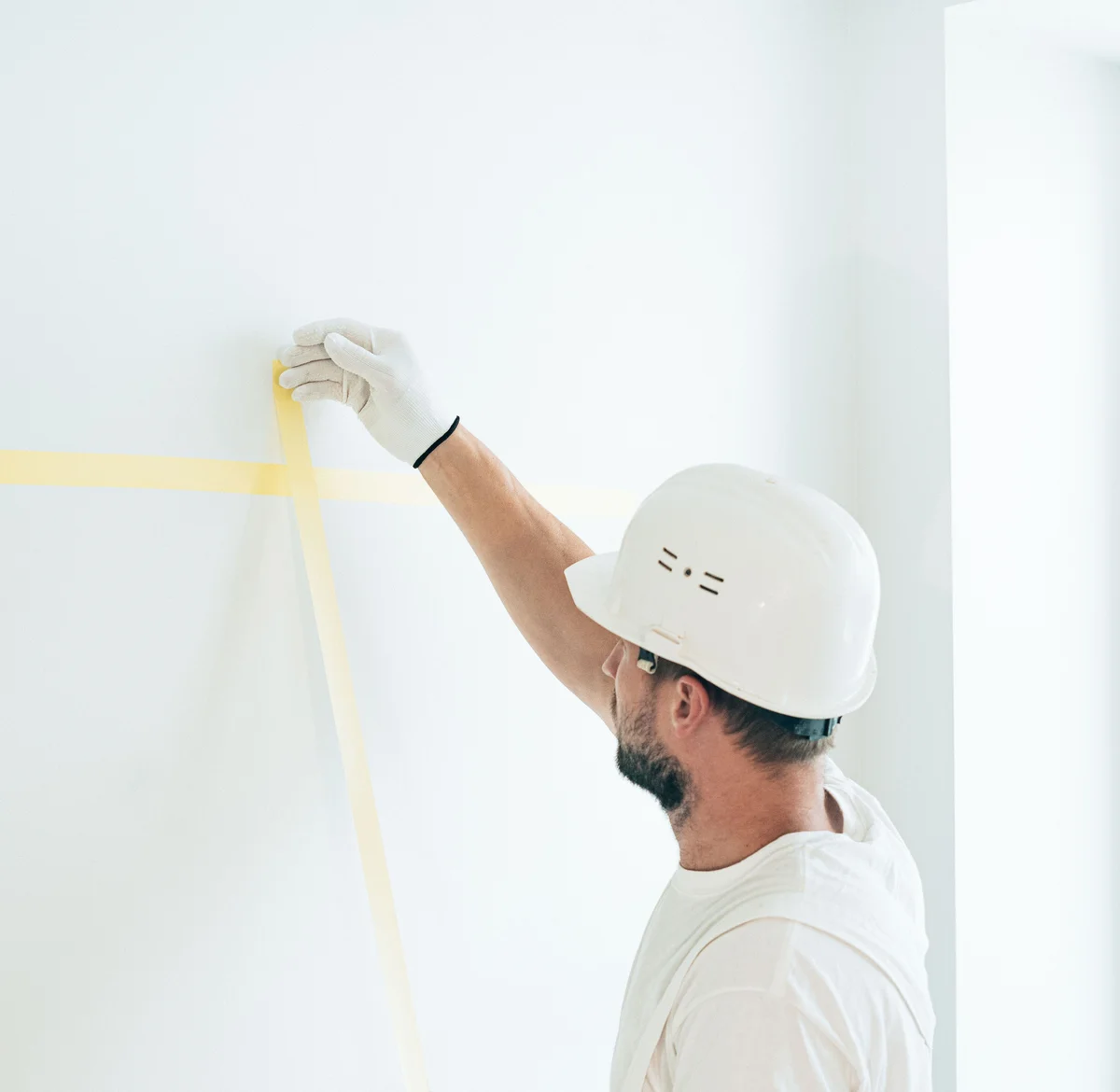 A decorator applies yellow painter’s tape to a wall wearing white gloves