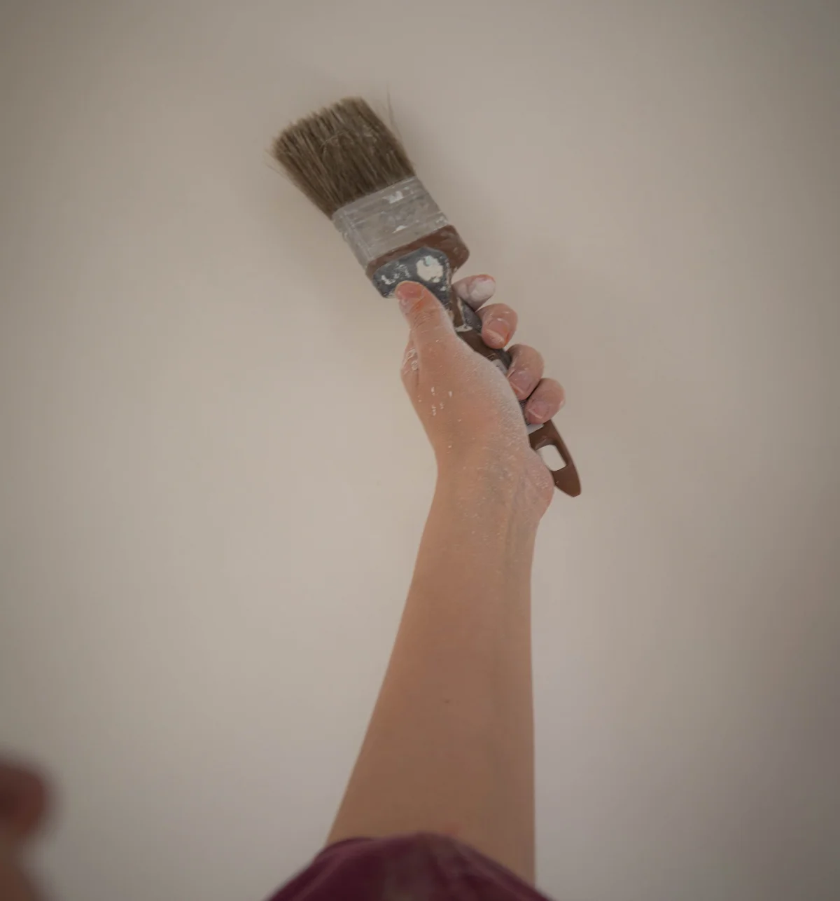 A hand holds up a paintbrush against a white wall