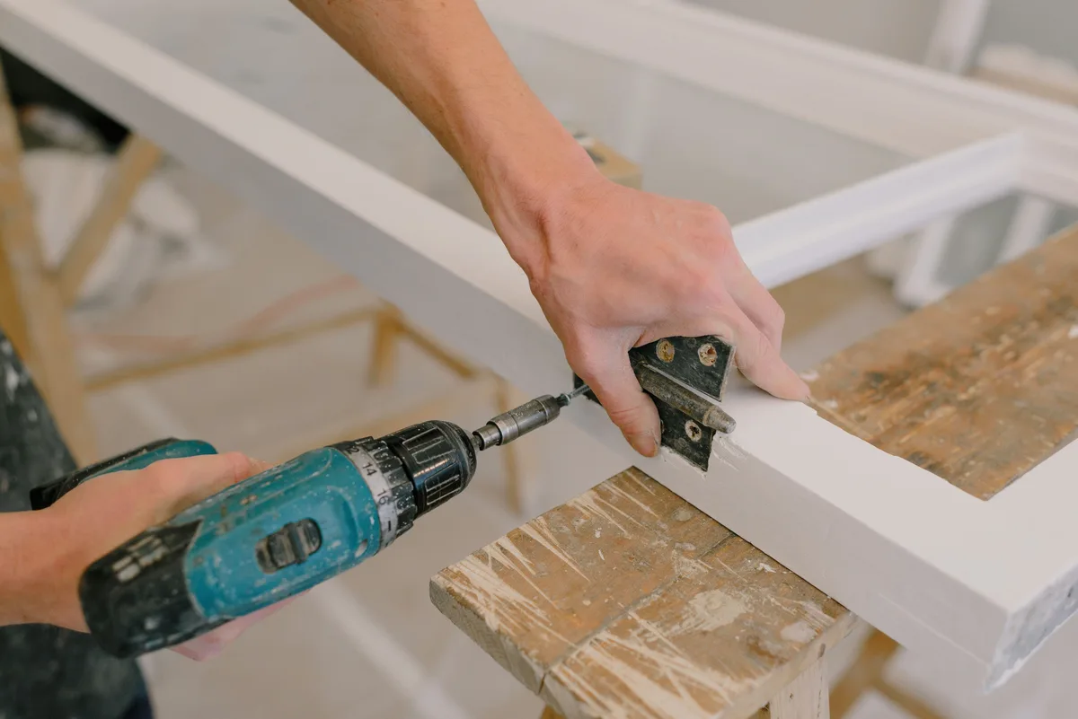A hand and a drill at a hinge being fitted to a white door