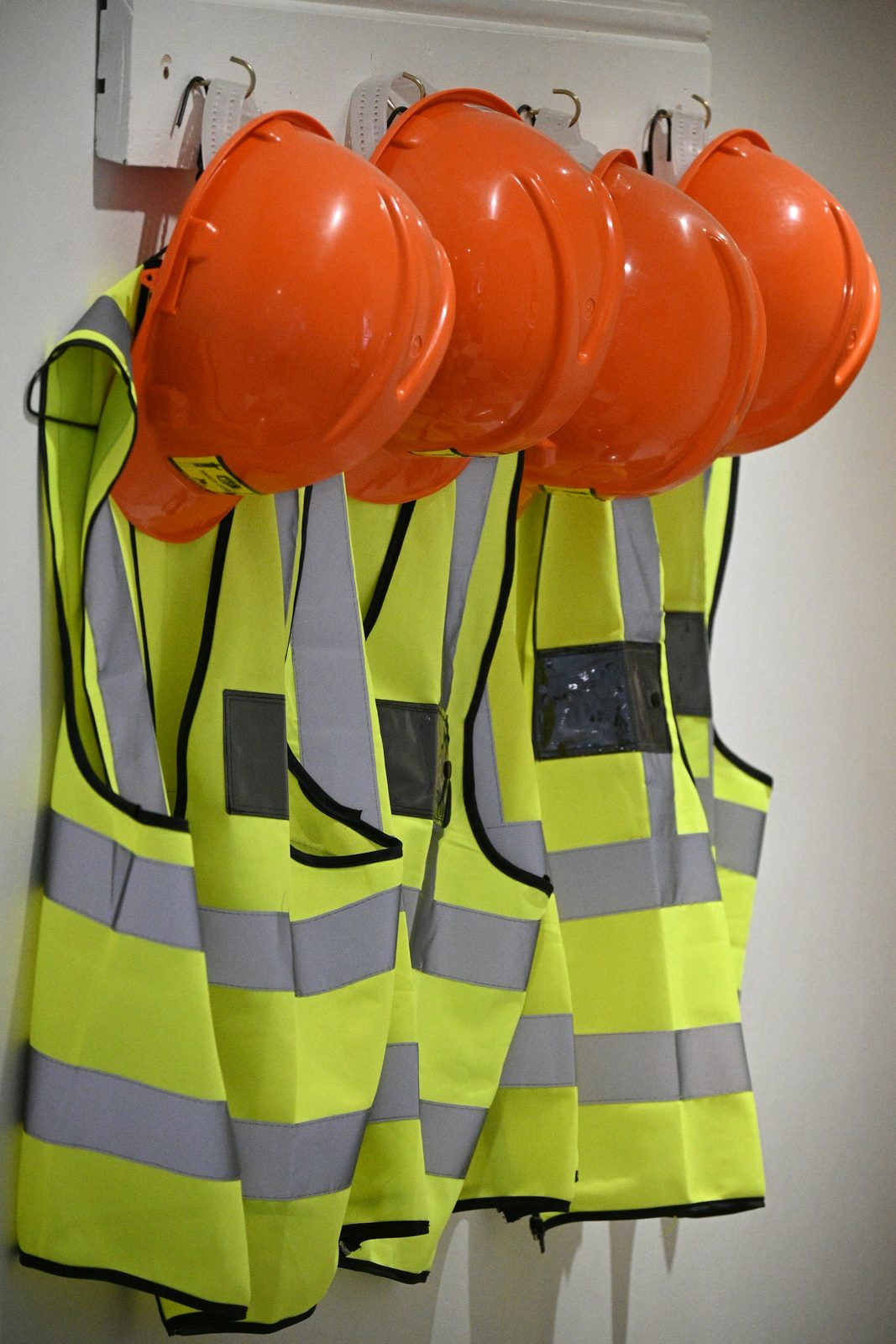 Orange safety helmets and yellow high-visibility vests hanging on a coat rack