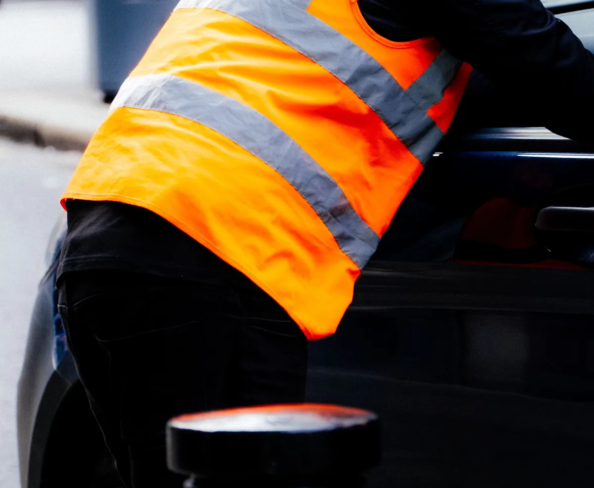 Werker in een oranje waarschuwingshesje met twee horizontale reflecterende banden rond de romp