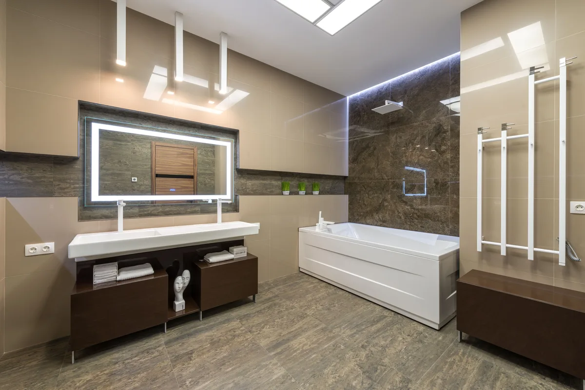 Spacious bathroom with an illuminated LED mirror above a double basin, a bath and a light strip along the ceiling