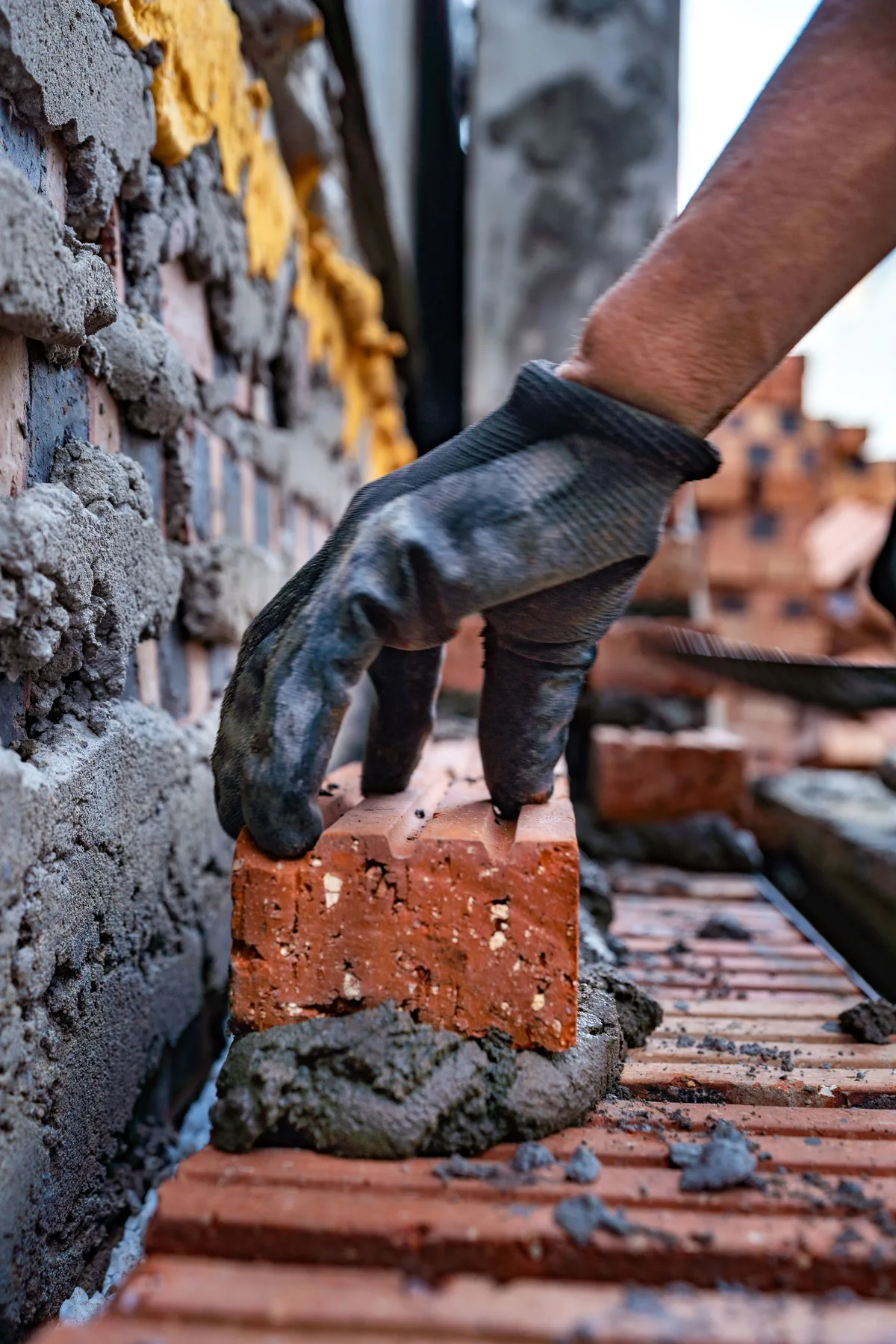 Hand in a work glove placing a red brick into wet mortar on a small wall