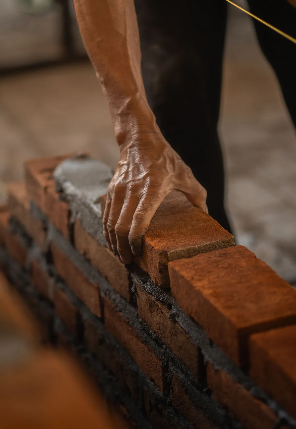 Hand placing a red brick onto a bed of grey mortar during bricklaying