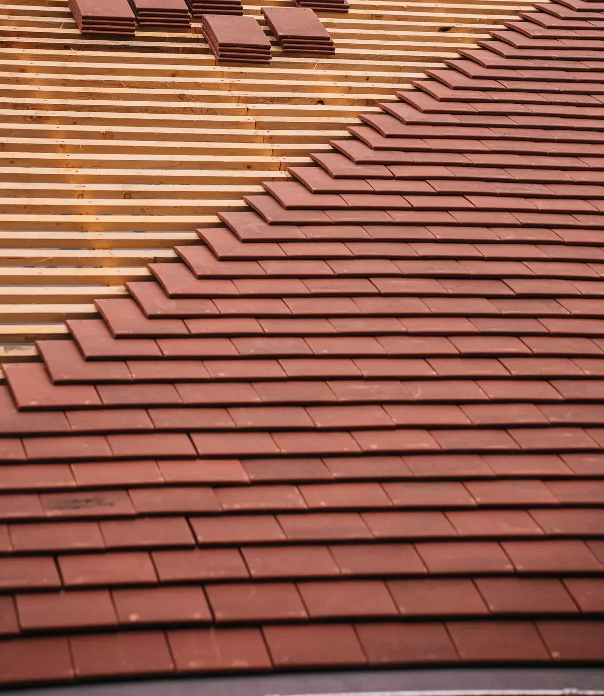 Red roof tiles overlapping on timber battens, with part of the roof not yet tiled