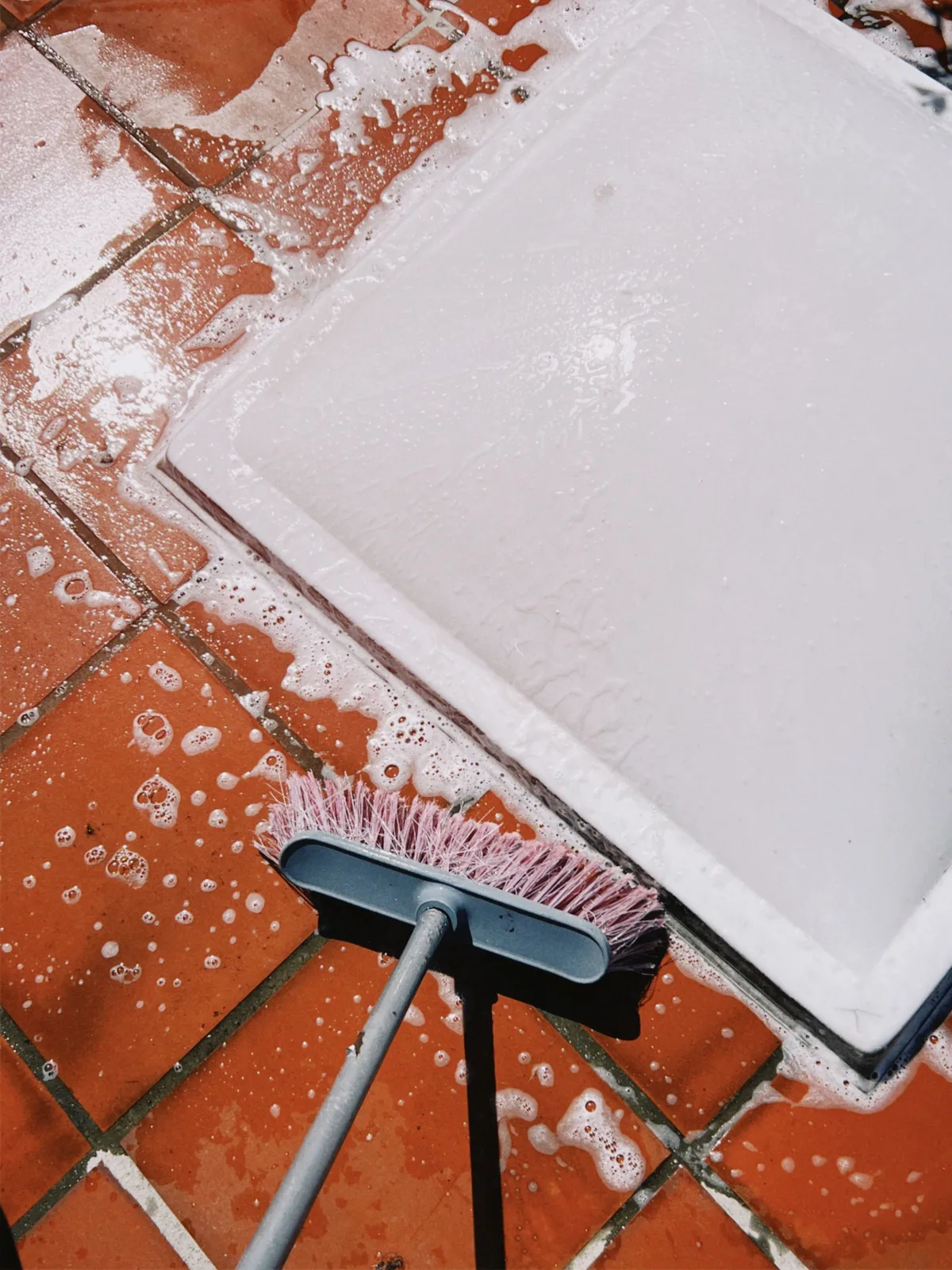 Red patio tiles being scrubbed with soapy water and a stiff brush
