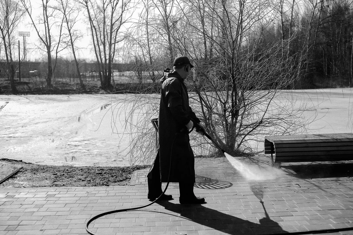 Black and white photo of a man cleaning brick paving with a pressure washer
