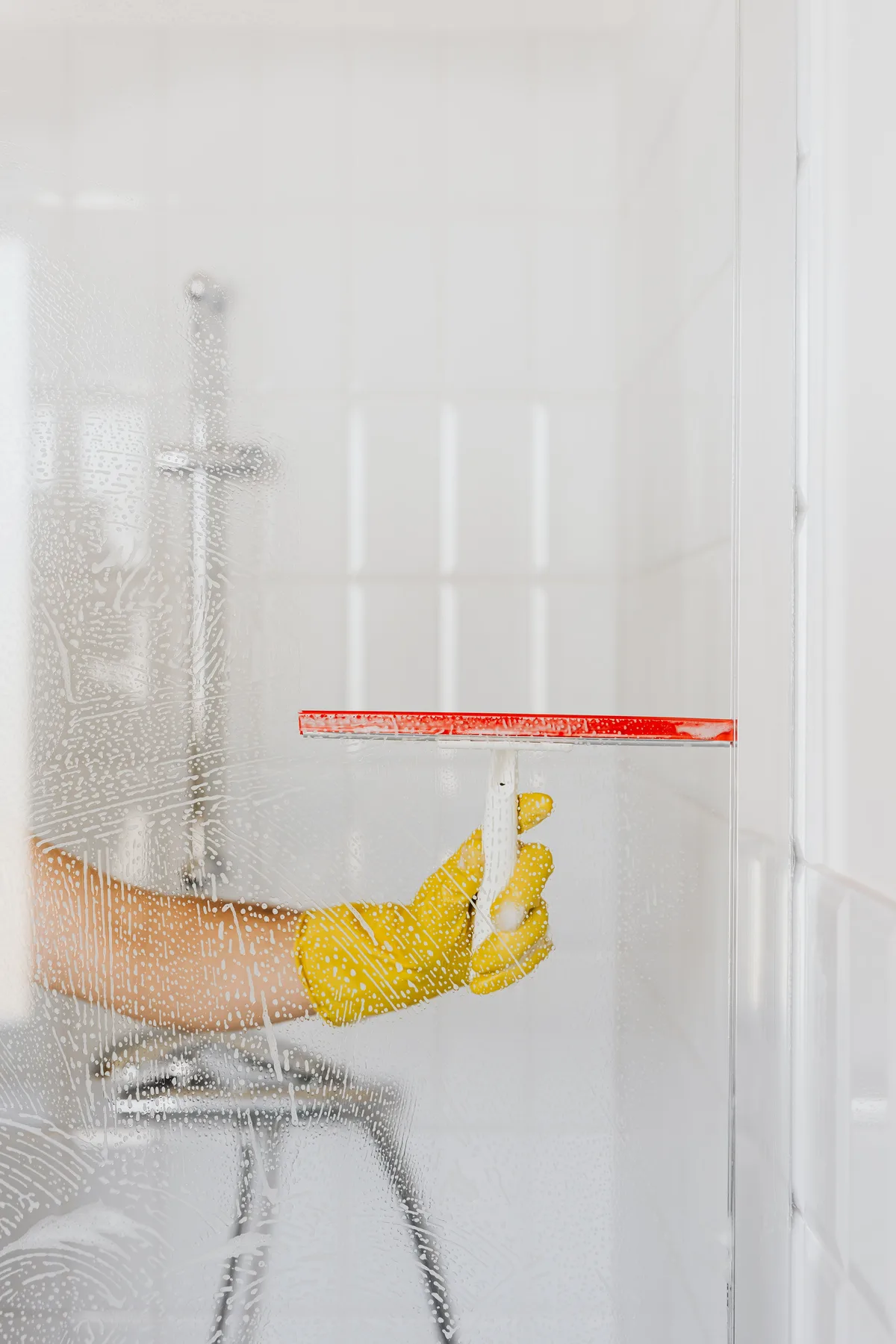 Hand in a yellow glove wiping a glass shower screen dry with a squeegee