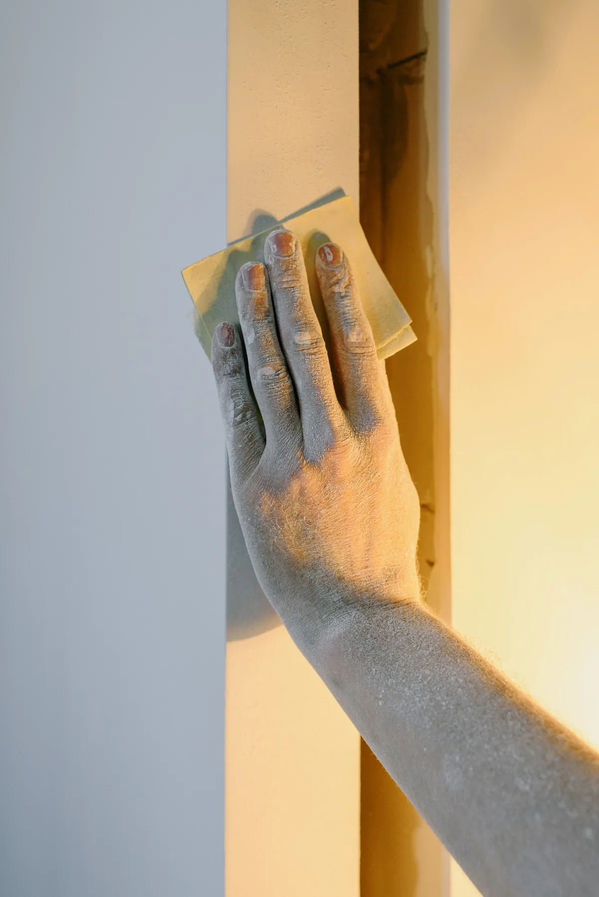 A hand sands a wall with sandpaper