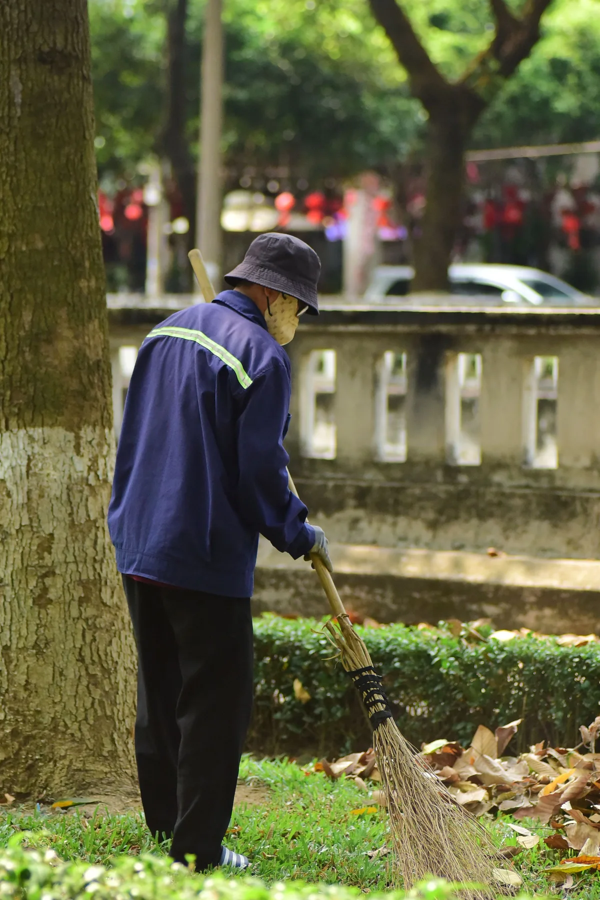 A gardener sweeps up leaves in a park with a broom