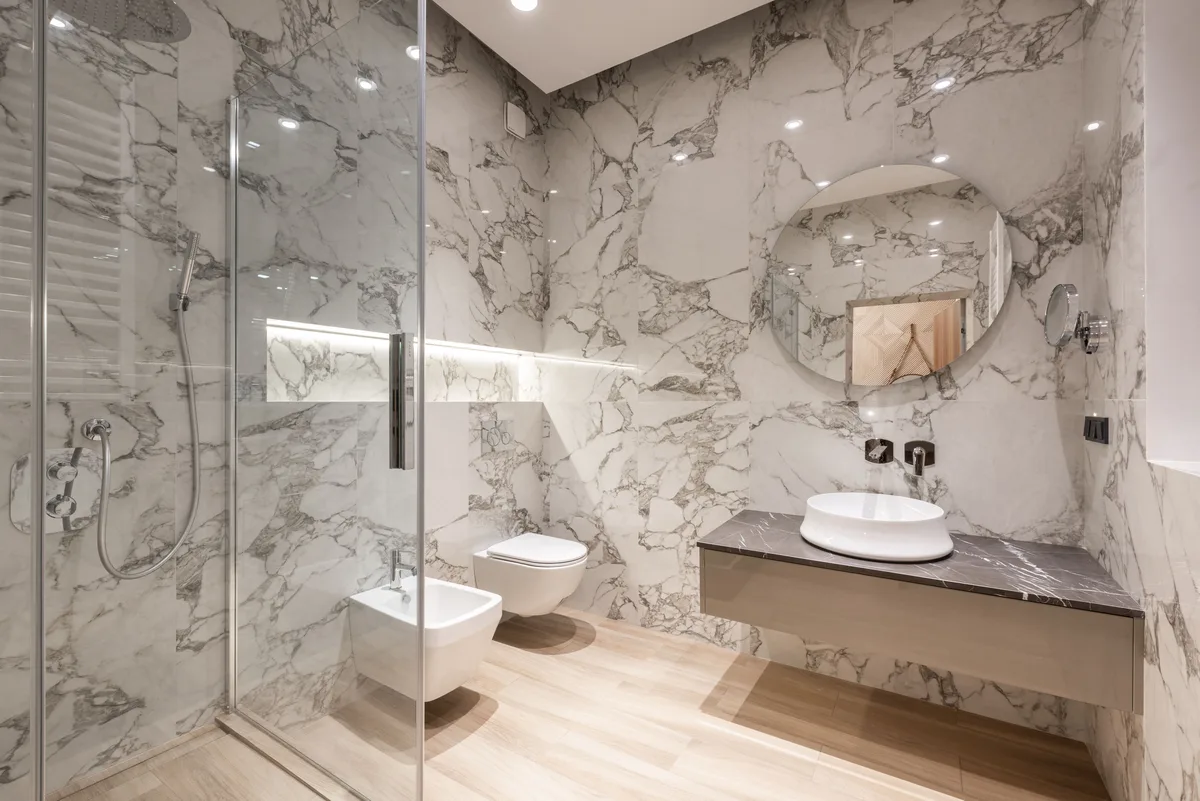 Marble bathroom with a large round mirror above a floating vanity top with a white basin