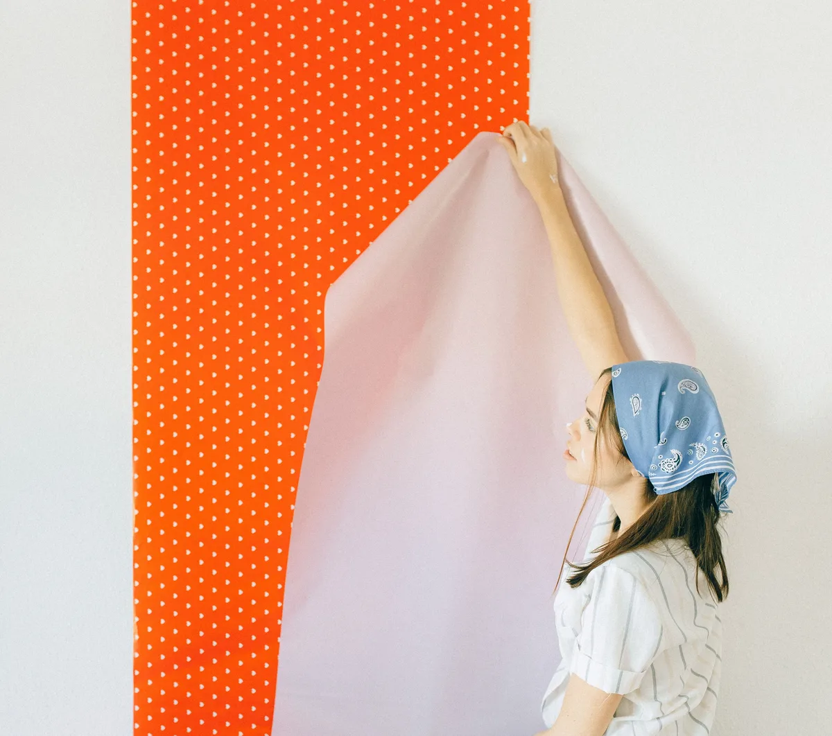 Vrouw zet een nieuwe baan roze behang tegen de muur naast een rode baan met witte stippen