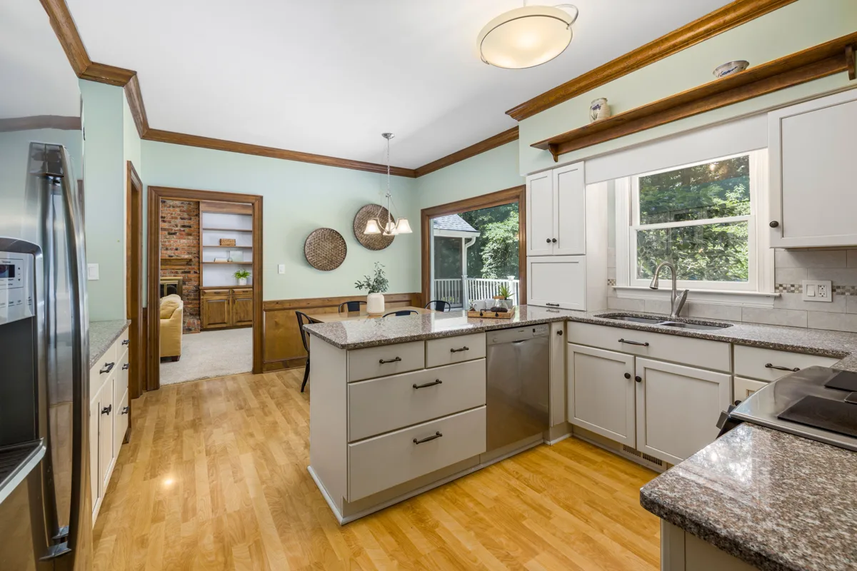 A kitchen with light cabinets, a granite worktop and a sink under a window