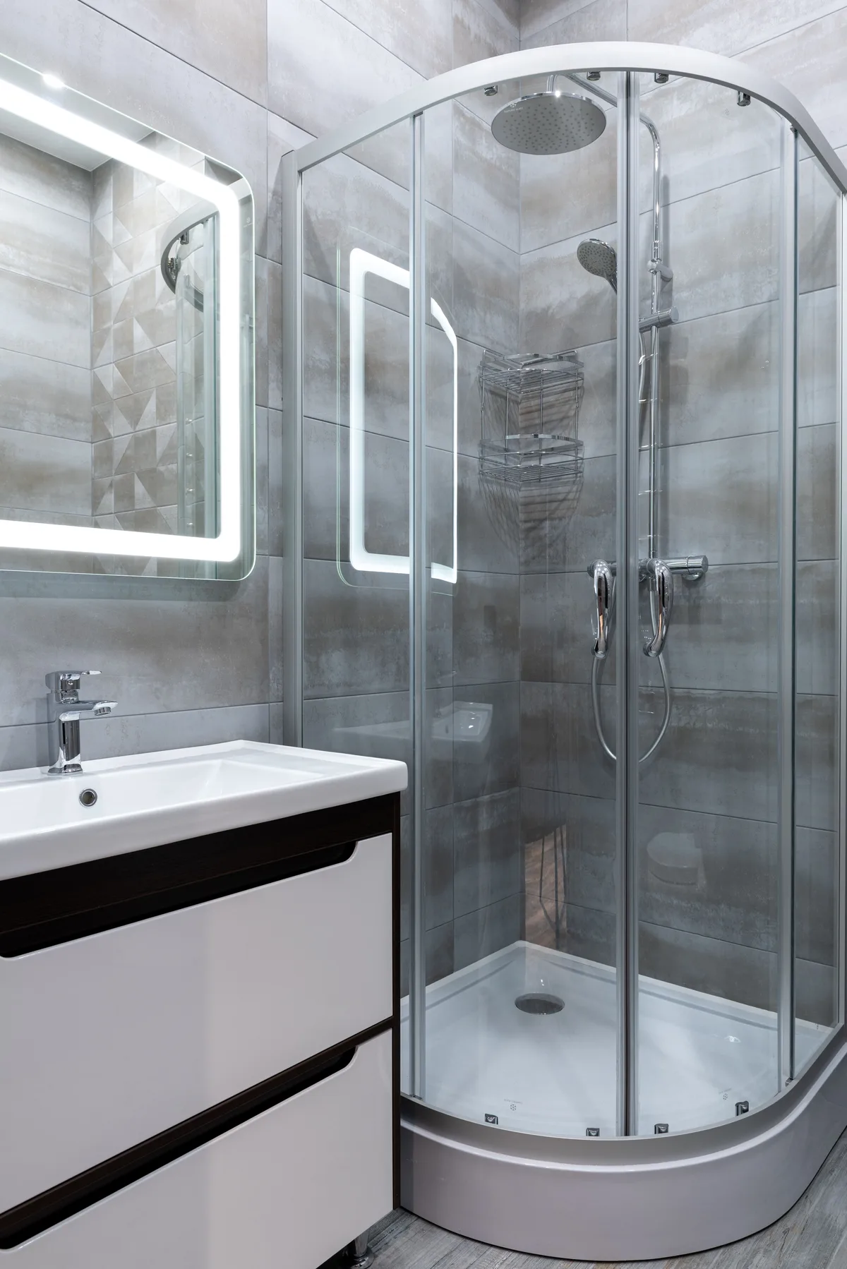 A round glass shower cabin next to a vanity unit with an illuminated mirror