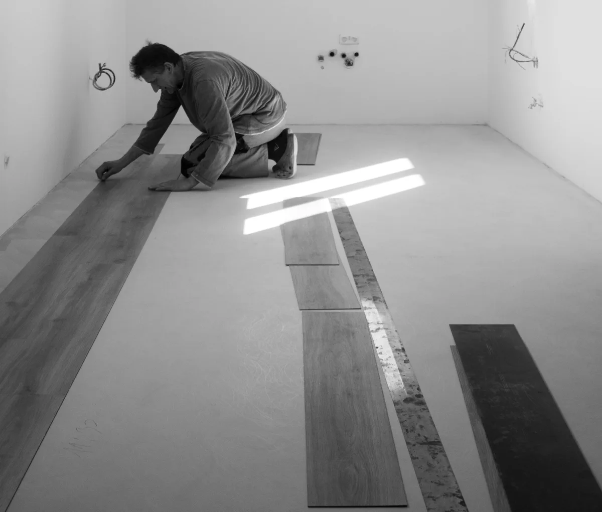 Man on his knees laying out vinyl planks in rows on a level subfloor in an empty room