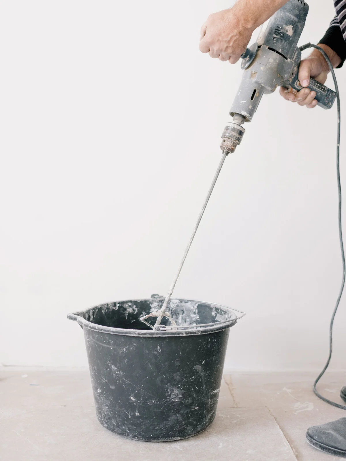 A DIYer mixing levelling compound or mortar in a bucket with a drill and mixing paddle