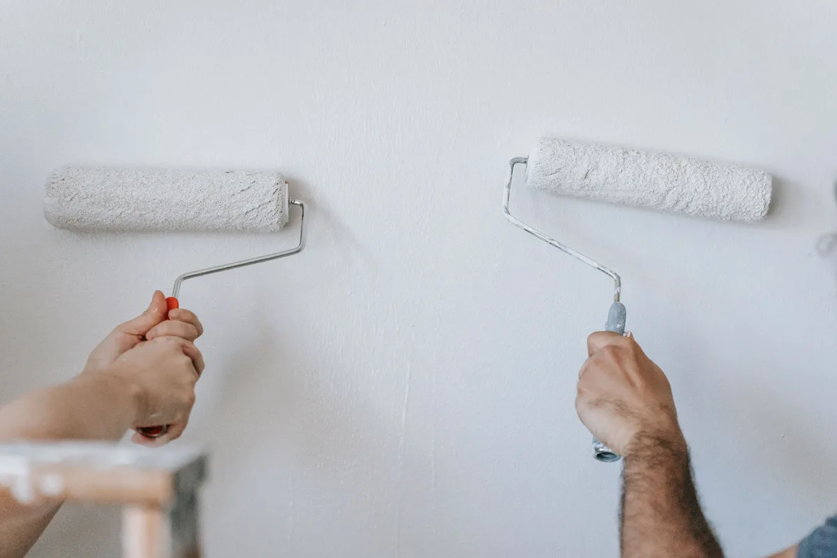 Two people paint a white wall with paint rollers