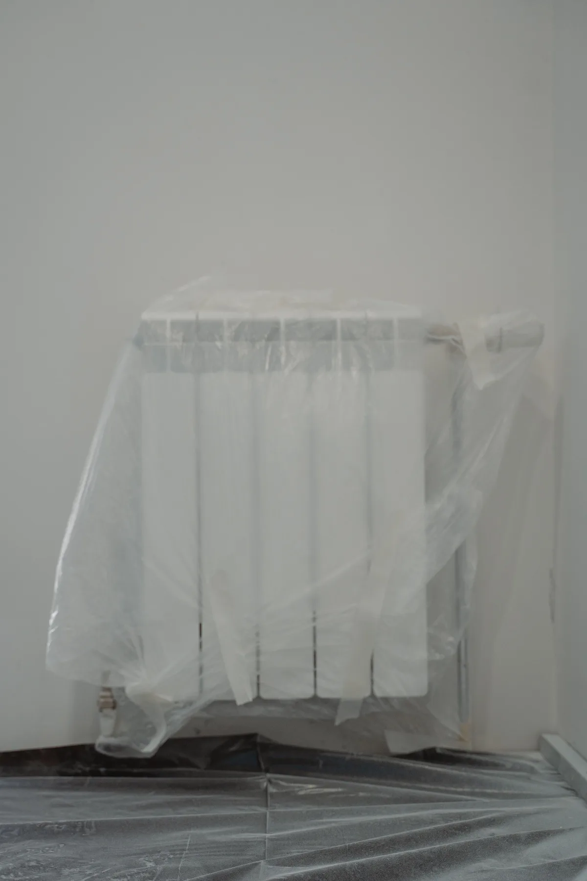 A radiator wrapped in clear film, with the floor below covered with protective sheeting during a renovation