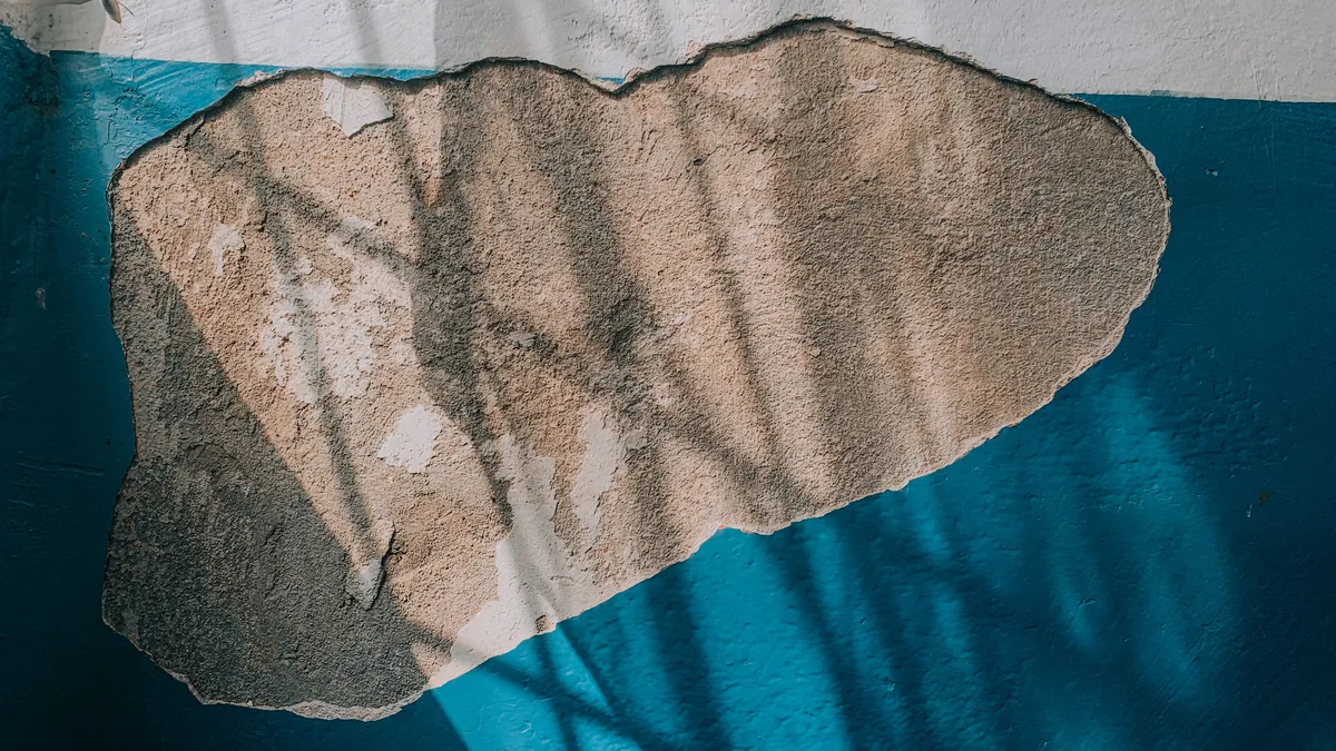 Damaged plaster: a section of plaster that has come away from a blue painted wall
