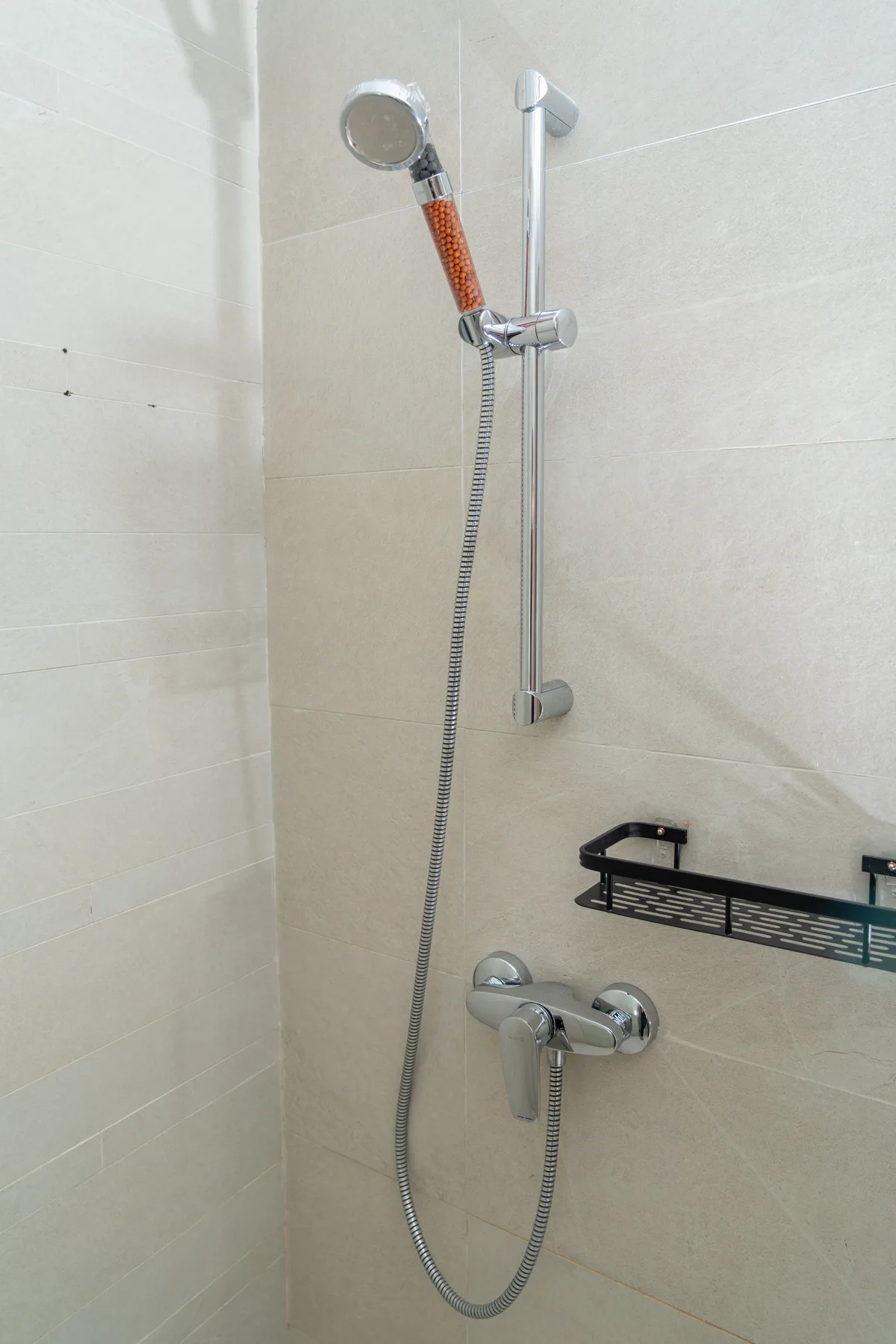 A hand shower with hose on a slide rail against a light tiled wall
