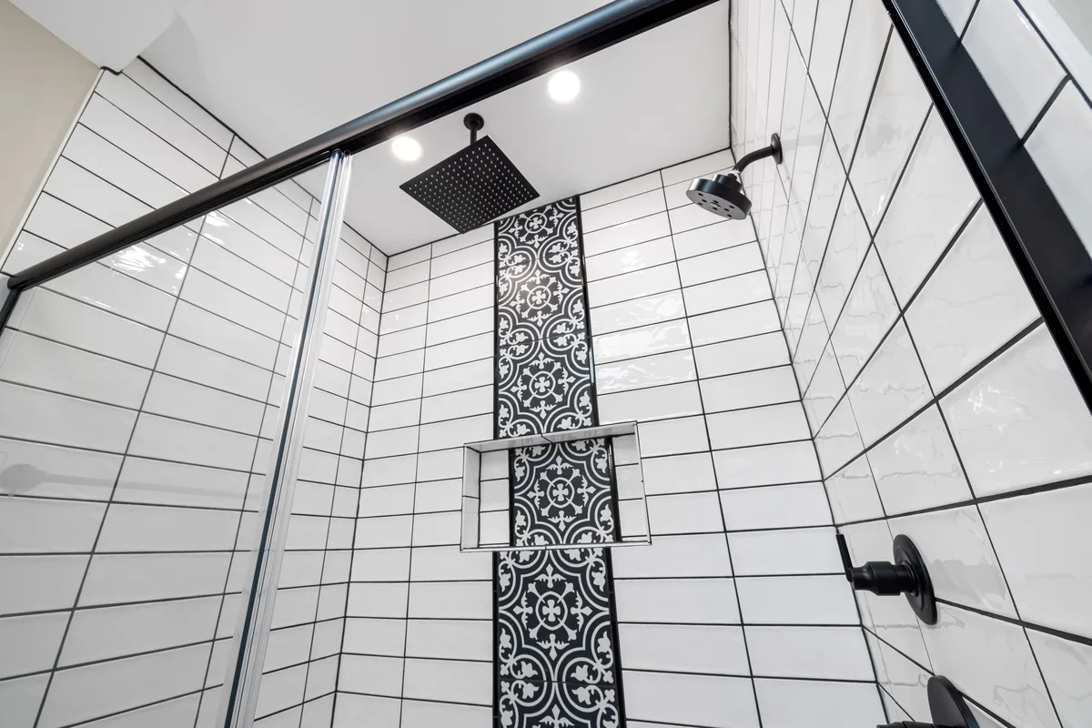 A shower with white tiles and a patterned tile strip