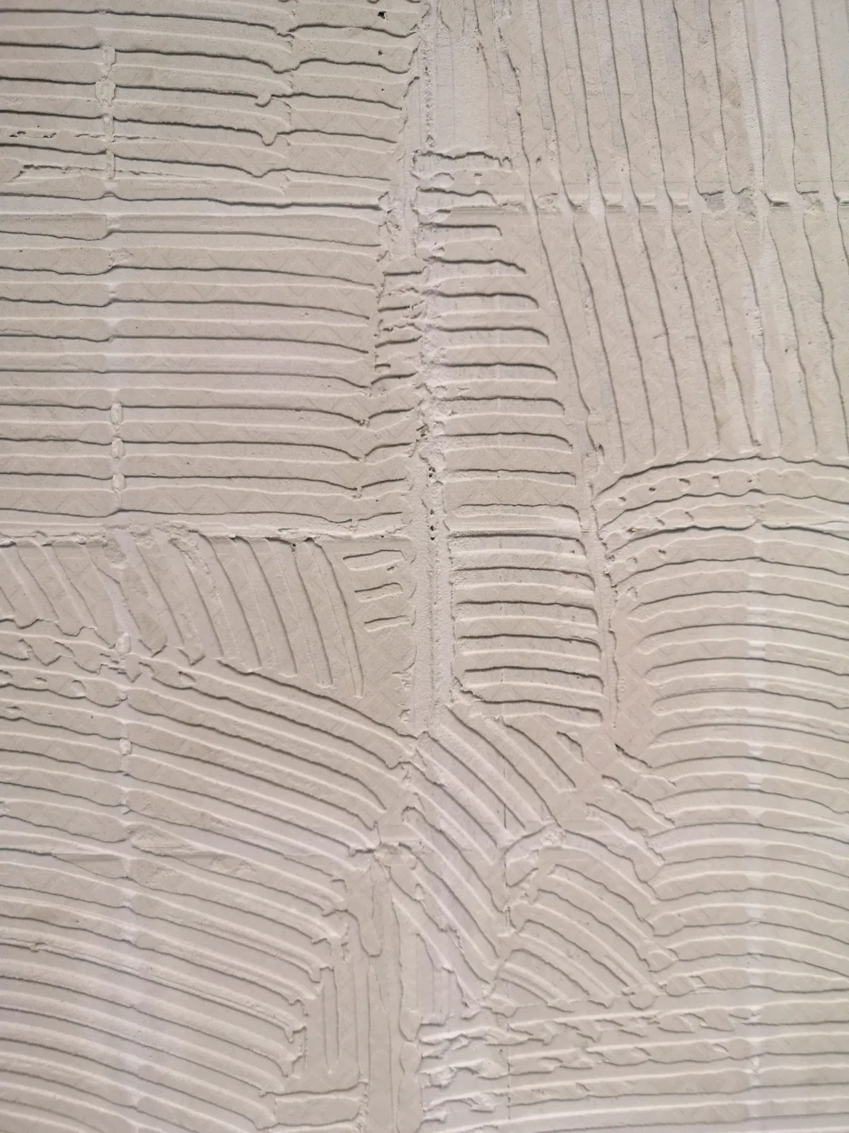 Light-coloured wall with tile adhesive in combed ridges