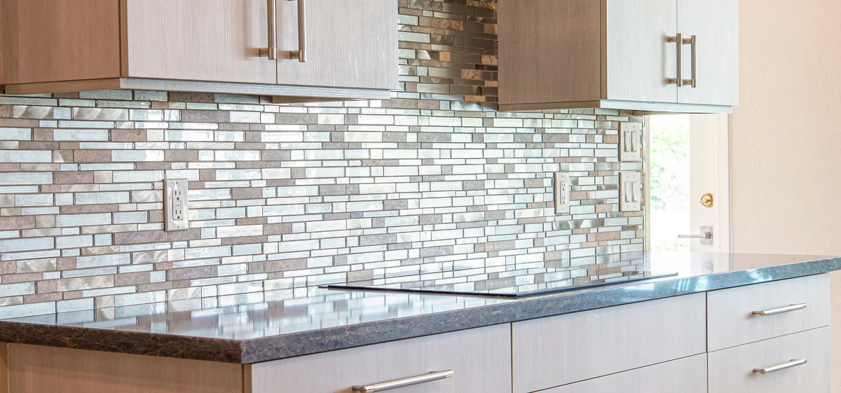 Kitchen splashback of narrow mosaic strips between the wall cabinets and the worktop, with sockets in the tiling