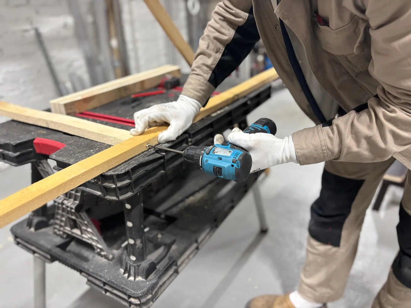 A DIYer drilling a hole in a wooden batten on a workbench with a cordless drill driver