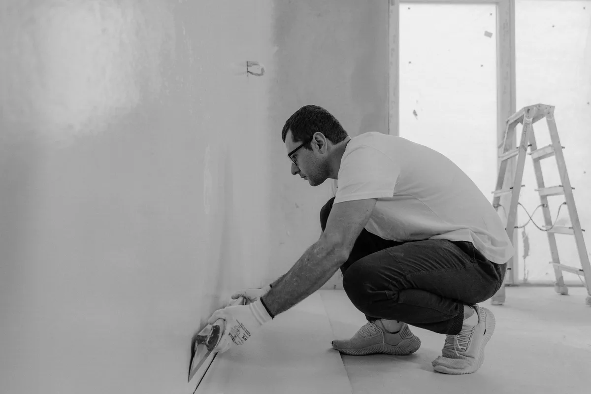 A DIYer in black and white finishing a wall with a plastering trowel