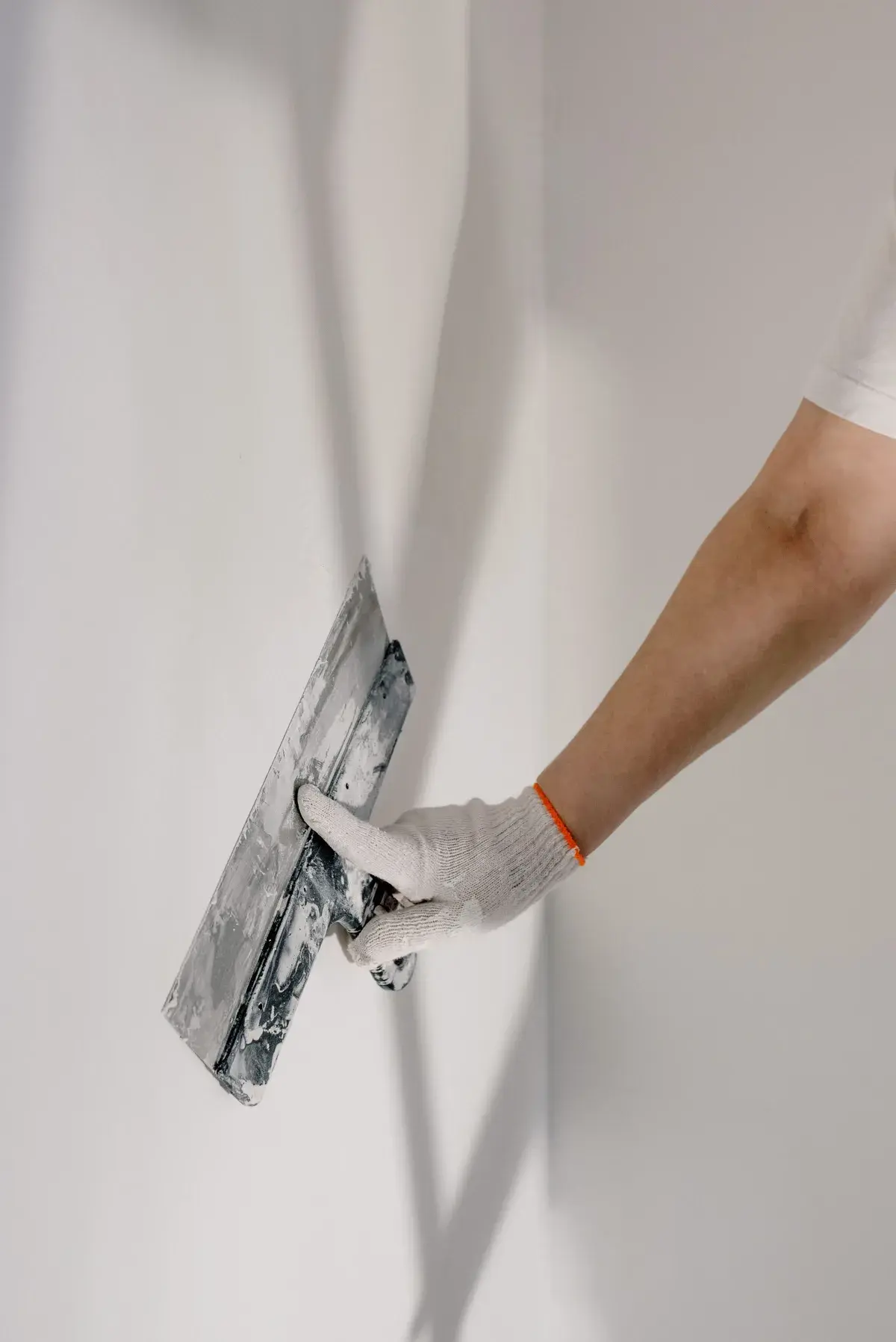 A gloved hand smooths a wall with a plastering trowel