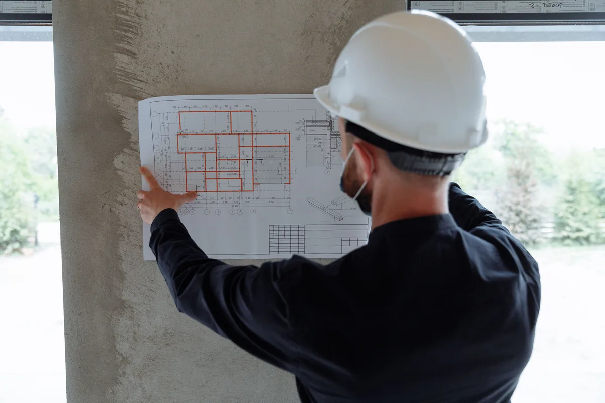Ingenieur met witte helm houdt een plattegrond tegen een betonnen kolom