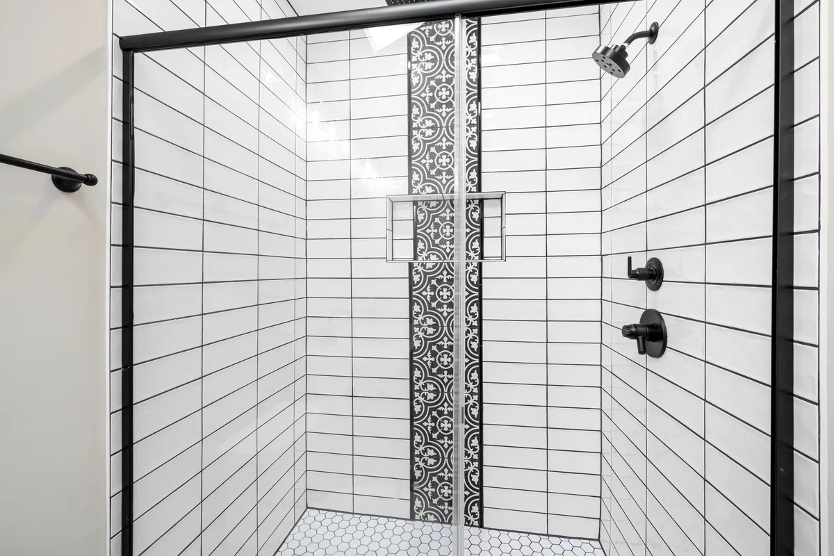 Shower with white rectangular wall tiles in a stack bond with dark grout joints and a decorative strip