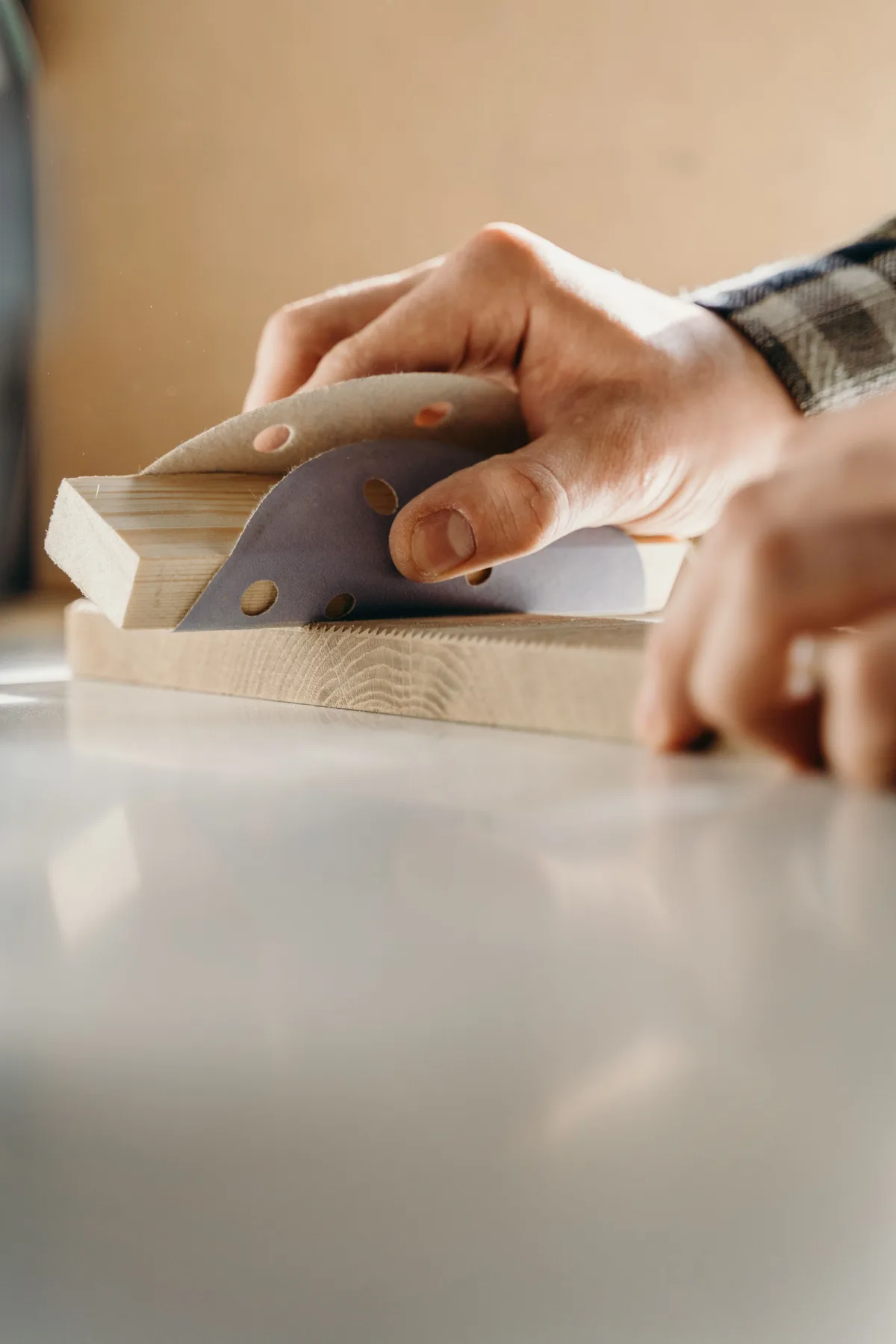Person sanding a piece of wood with sandpaper on a workbench