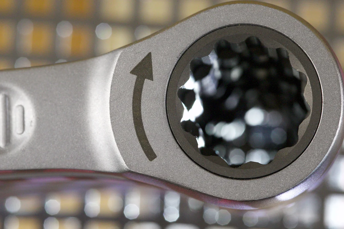 Close-up of the ring head of a silver ratchet wrench with direction arrow