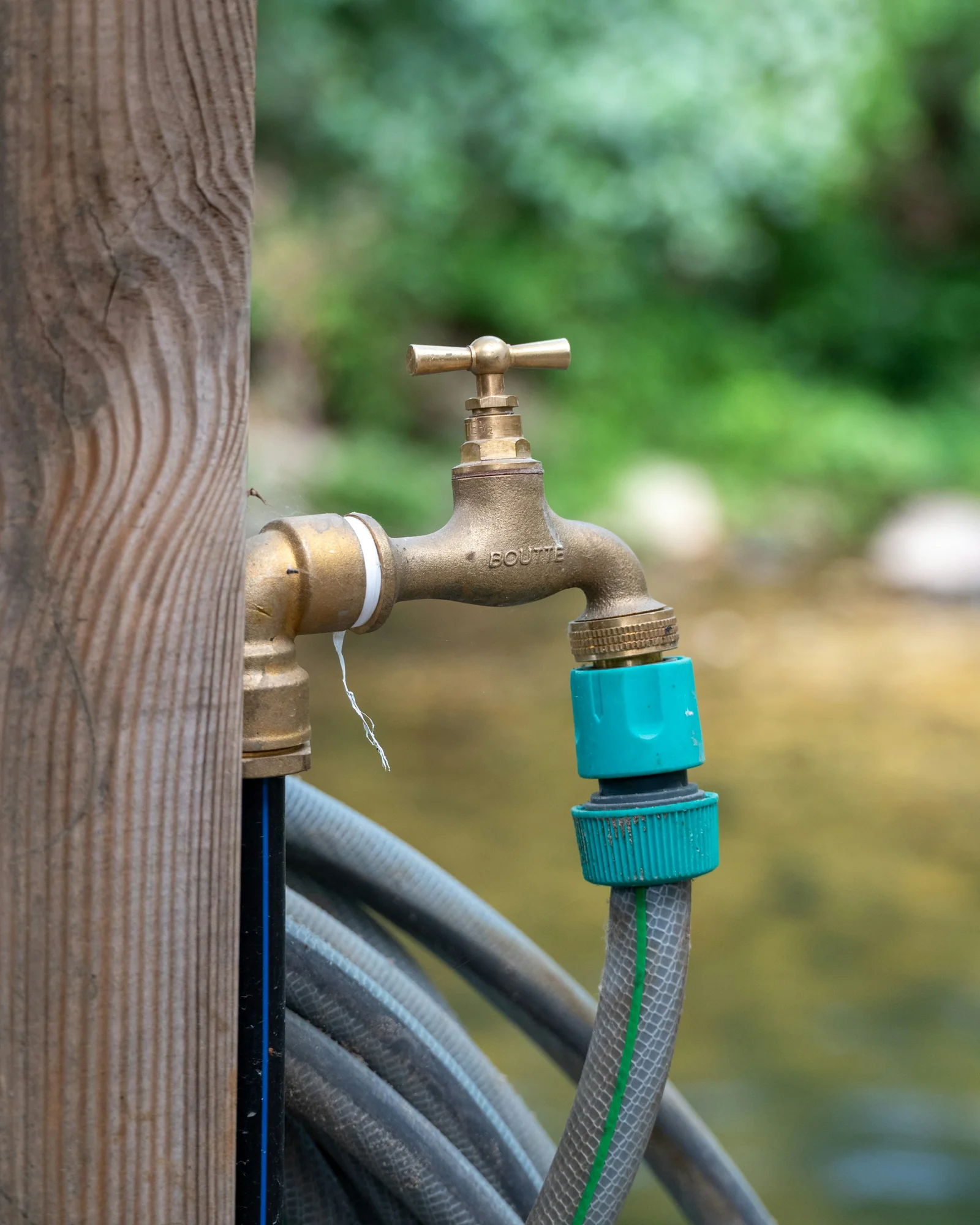 Brass outdoor tap on a wooden post with a garden hose attached