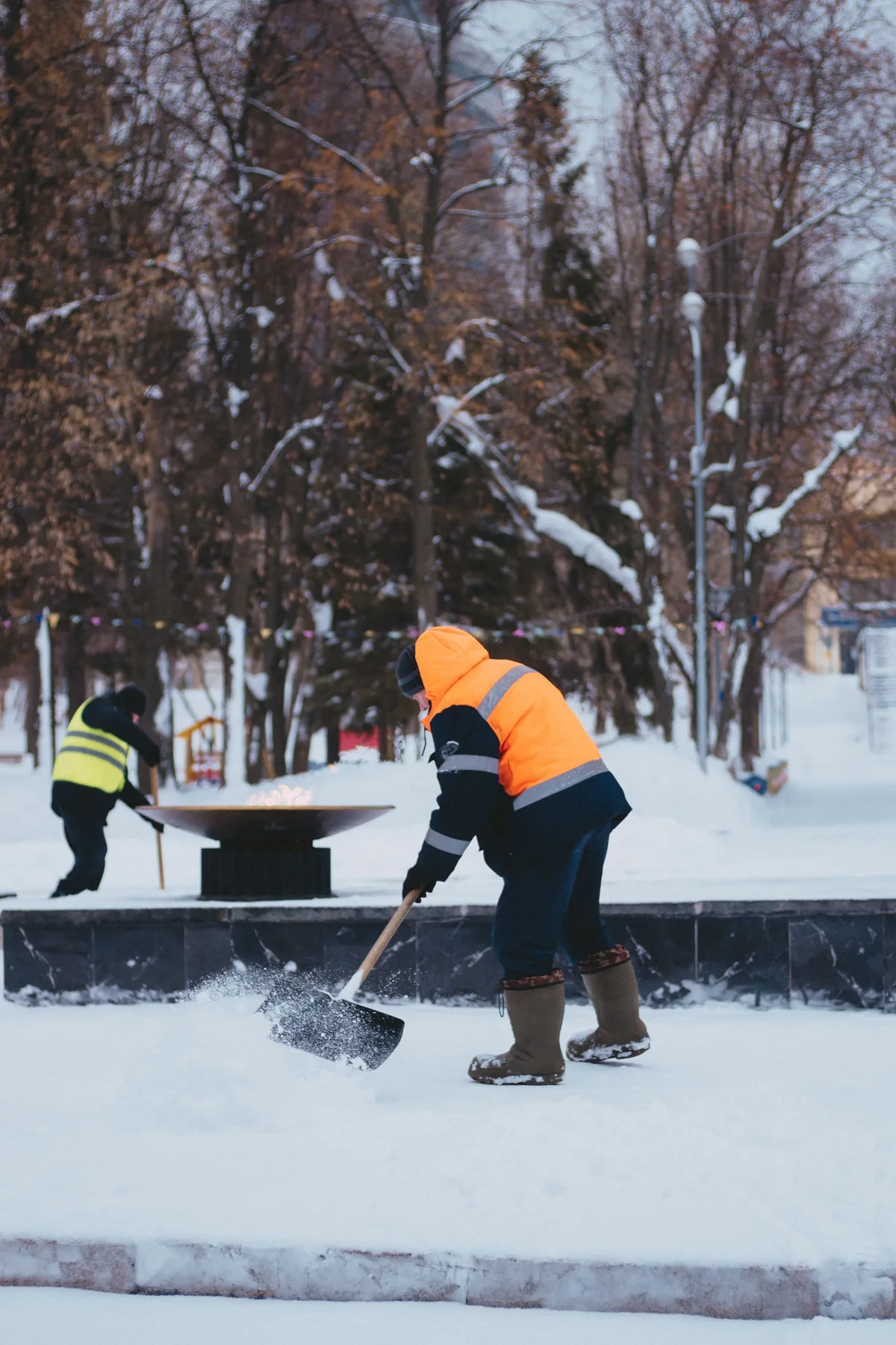 Man in een oranje jas schept sneeuw op een pad