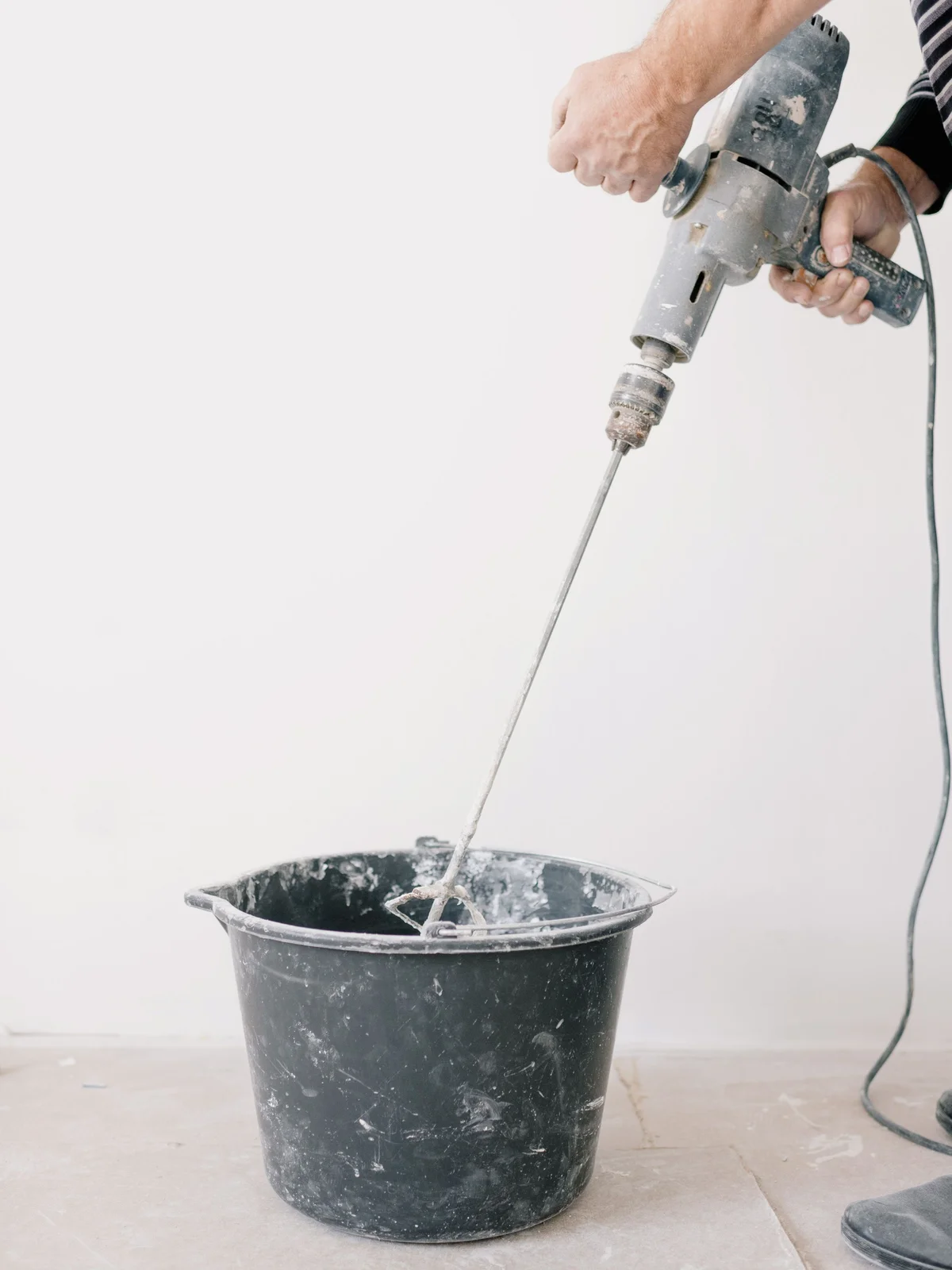 A person mixes mortar in a black bucket with a mixer on a drill